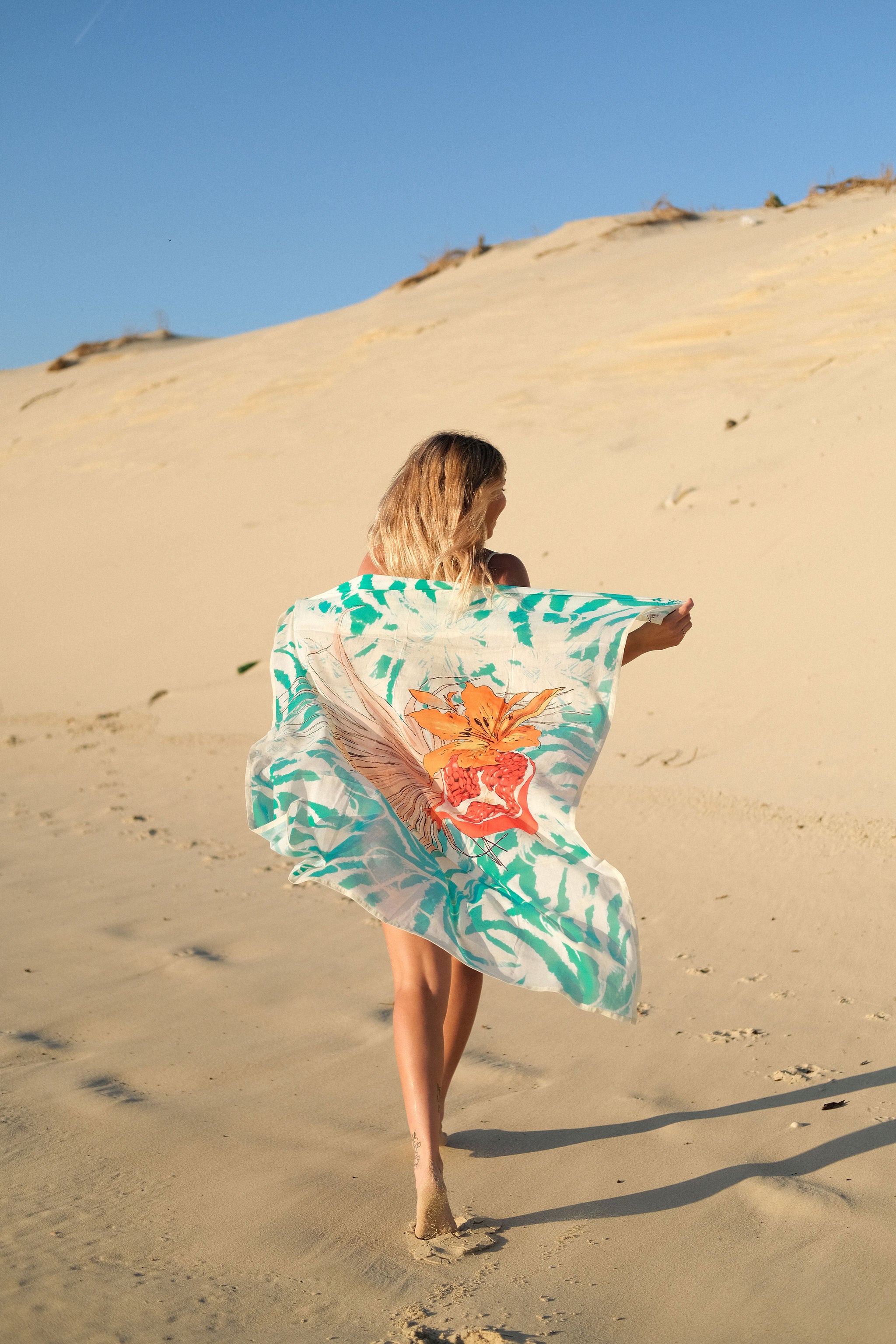 Femme portant le paréo Palma Granada turquoise dans les dunes au coucher du soleil